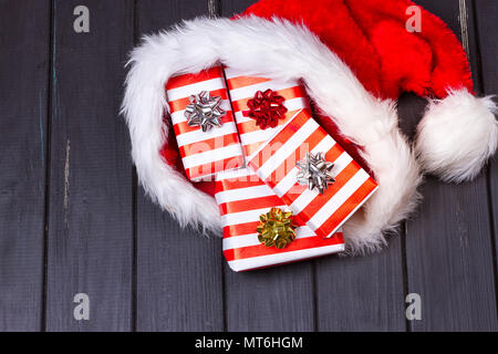 Weihnachten Geschenke in einem Weihnachtsmann Hut auf schwarzem Holz Hintergrund Stockfoto