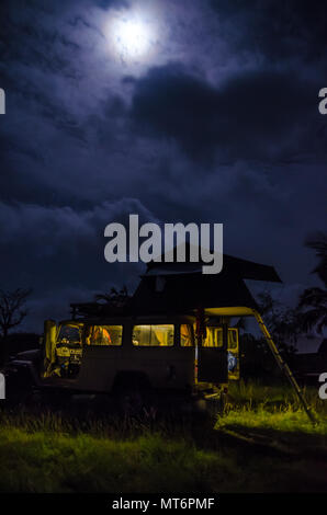 4x4 Geländewagen mit Dachzelt und das innere Licht während der Nacht mit bewölktem Himmel und starken Mond, camping Konzept Stockfoto