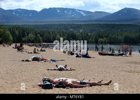 In den letzten Flecken des Schnees bleiben auf die Cairngorms, wie Leute das heiße Wetter auf dem höchsten Strand in Großbritannien in der Nähe von Aviemore am Loch Morlich genießen, wie Briten sehen konnte der heißeste Tag des Jahres dieser Feiertag Montag. Stockfoto