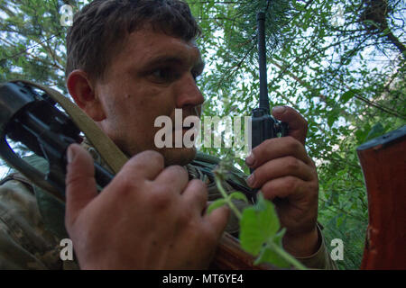 Eine ukrainische Soldaten bis zum gegnerischen Streitmacht an der Yavoriv Combat Training Center Funkgeräte ein Bericht zu seinem Zugführer, als er reconnoiters Positionen entlang der Flanke des 1 Airmobile Bataillon, 79 Air Assault Brigade in der Dämmerung des 29. Juni während des Bataillon kulminieren Kraft - Kraft der Übung, die Grube das Bataillon gegen die gegnerische Streitmacht an der Yavoriv Combat Training Center auf dem internationalen Friedens und der Sicherheit, in der Nähe der Yavoriv, Ukraine zugeordnet. (Foto von Sgt. Anthony Jones, 45th Infantry Brigade Combat Team) Stockfoto