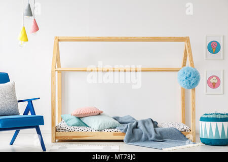 DIY-Bett aus Holz, Kissen und Decke, Lampen, blaue Sessel, Puff und Eis Poster in ein Kinderzimmer Innenraum Stockfoto