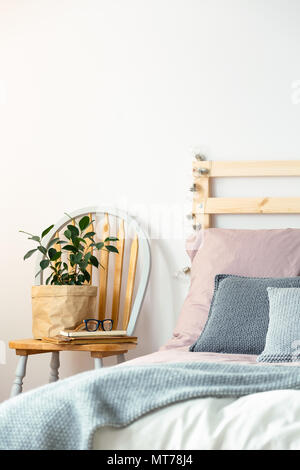 Anlage auf hölzernen Stuhl am Bett mit blauen Decke in Pastelltönen Schlafzimmer Innenraum. Real Photo Stockfoto