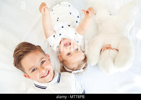 Positive Kinder lächeln lag auf einem weißen Bett. Stockfoto