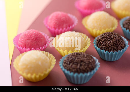 Brasilianische Spezialitäten: Brigadeiro, Beijinho und Bicho de Pe. Kindergeburtstag. Candy Kugeln in einer geraden Linie. Bunter Hintergrund. Stockfoto