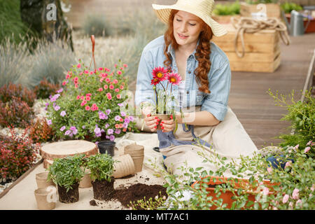 Junge Frau mit einem Blumentopf, Bepflanzung und auf der Suche nach Ihrem Haus Garten von der Terrasse Stockfoto