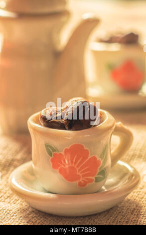 Kaffeebohnen in einer schönen kleinen Porzellan Tassen close-up. Starker Kaffee Poster. Stockfoto