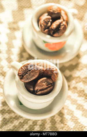 Kaffeebohnen in einer schönen kleinen Porzellan Tassen close-up. Starker Kaffee Poster. Stockfoto