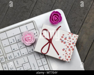 Blick von oben auf die Rosen, weißer Laptop und roter Geschenkbox für den Hintergrund. Stockfoto