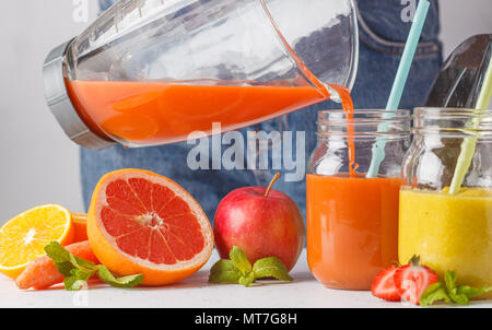 Frau kocht mehrfarbig Sommer Fruchtsäfte oder Smoothie in Gläsern und Zutaten auf weißer Tisch. Stockfoto