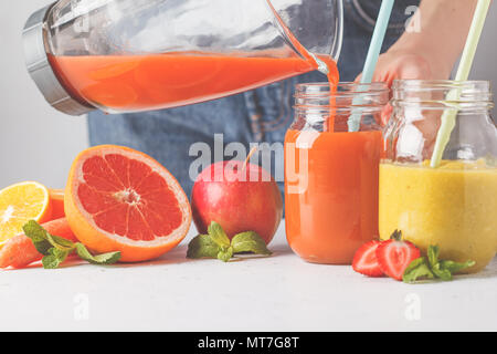 Frau kocht mehrfarbig Sommer Fruchtsäfte oder Smoothie in Gläsern und Zutaten auf weißer Tisch. Stockfoto