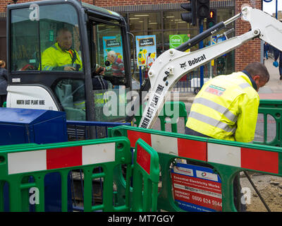 Handwerker Betrieb eines kleinen Bobcat Bagger Graben in der Fahrbahndecke, die für die Installation eines elektrischen Kabel Stockfoto