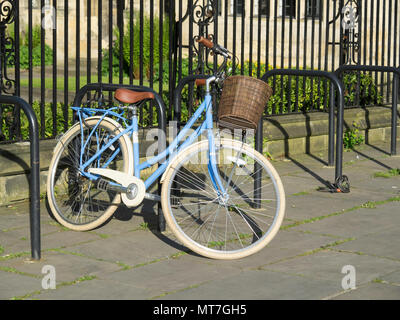 Eine blaue Damen Fahrrad mit einem offenen hinteren Träger und einem Korb am Lenker zu Geländer gesperrt Stockfoto