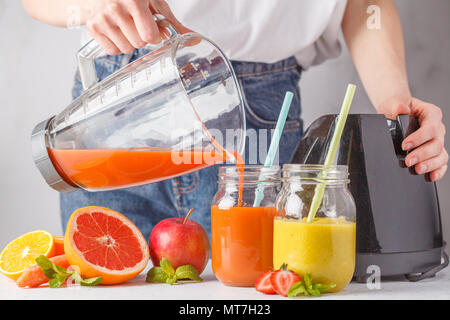 Frau kocht mehrfarbig Sommer Fruchtsäfte oder Smoothie in Gläsern und Zutaten auf weißer Tisch. Stockfoto