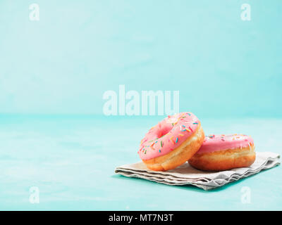 Zwei rosa Donuts auf der blauen konkreten Hintergrund mit kopieren. Bunte Donuts mit Copyspace. Glasierte Krapfen mit Streuseln Stockfoto