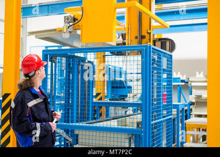 Arbeiter in einer Fabrik arbeiten trägt blaue Anzug und roter Helm suchen in Maschinen im Hintergrund Stockfoto