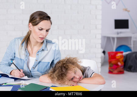Gelangweilte Kinder liegen mit dem Kopf auf dem Schreibtisch neben Hausaufgaben Stockfoto