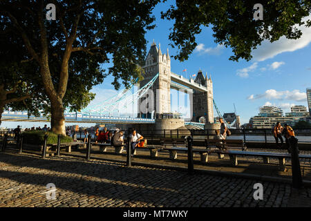 London, Großbritannien, 31. JULI 2017: Establishing Shot Wahrzeichen von London Tower Bridge. Abendlicht. Sportboote. Touristen sitzen auf der Bank ein Stockfoto