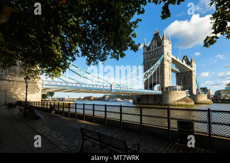 London, Großbritannien, 31. JULI 2017: Establishing Shot Wahrzeichen von London Tower Bridge. Abendlicht. Sportboote. Touristen sitzen auf der Bank ein Stockfoto