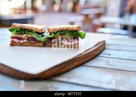 Handwerkliche Sandwich mit sortierten Bio Gemüse halbieren und ruht auf einem hölzernen Tisch in einem Straßencafé Stockfoto
