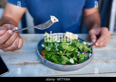 Junger Mann allein sitzen an einem bistrotisch Essen einen leckeren Teller mit gemischter Salat mit Messer und Gabel Stockfoto