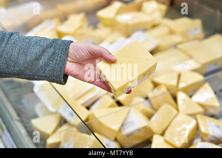 Hand des Käufers mit einem Stück Käse im Store. Stockfoto