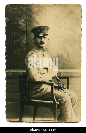 Deutsches Historisches Foto Karte: Ein Offizier in Uniform mit einem Schwert in der Hand auf einem Stuhl halb sitzenden - gedreht und posieren. Studio. Erster Weltkrieg 1914-1918 Stockfoto