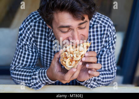 Hungrigen jungen Mann in einem Bistro sitzen, einen Bissen von seinem leckeren Erdnussbutter und Banane öffnen konfrontiert Sandwich Stockfoto