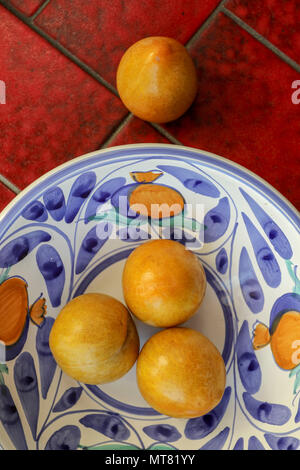 Gelbe Pflaumen in Weiß und Blau Schüssel auf eine rote Fliese Hintergrund Stockfoto