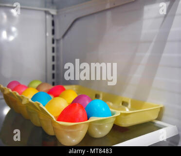 Ein Styropor ei sitzt geöffnet im Kühlschrank mit einem Dutzend bunt gefärbte gekochte Eier für das Osterfest. Stockfoto