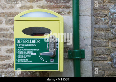 Automatisierter externer Defibrillator (AED). Notfall lebensrettende medizinische Ausrüstung in ein an der Wand montierter Schrank, in einem ländlichen Dorset Village entfernt. England. Stockfoto