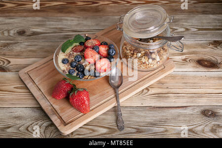 Müsli mit Nüssen, Joghurt, frische Blaubeeren und Erdbeeren in eine Glasschüssel auf einer hölzernen Hintergrund Stockfoto