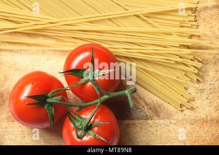 Rohe Spaghetti und ein paar frische Tomaten liegen auf Holzbrett Stockfoto
