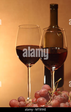 Trauben und zwei Weingläser in der Nähe der Flasche Rotwein auf braunem Hintergrund Stockfoto