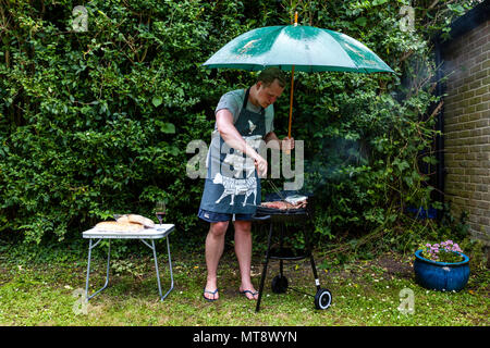 Lewes, Sussex, UK. 28. Mai 2018. Ein junger Mann kocht das Essen auf einem Grill während einer Regendusche. Credit: Grant Rooney/Alamy leben Nachrichten Stockfoto