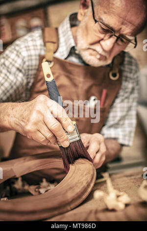 Ältere Tischler verwendet eine Bürste auf eine unvollendete Stuhl Stockfoto