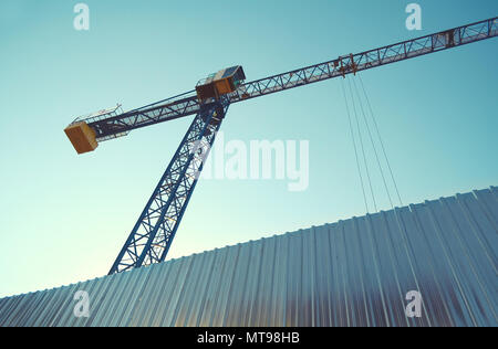 Baukran hinter Zinn Zaun auf wone den wolkenlosen Himmel, der Blick von unten nach oben. Stockfoto