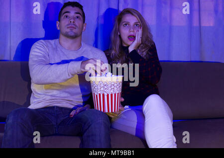 Junges Paar beobachten, Thriller Film im dunklen Zimmer mit Popcorn auf dem Sofa voll Aufmerksamkeit Stockfoto