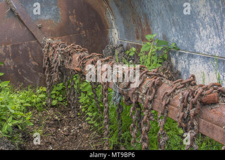 Blick in die Trommel eines Dreschkolbenstreuers mit Drehschlegelketten, dessen Unkraut in altem Dreck wächst - typische Landmaschinen und rostige Ketten. Stockfoto