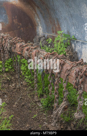 Blick in die Trommel eines Dreschkolbenstreuers mit Drehschlegelketten, dessen Unkraut in altem Dreck wächst - typische Landmaschinen und rostige Ketten. Stockfoto