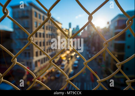 Downtown Manhattan und Chinatown gesehen durch eine chainlink Fence bei Sonnenuntergang auf der Manhattan Bridge. Stockfoto