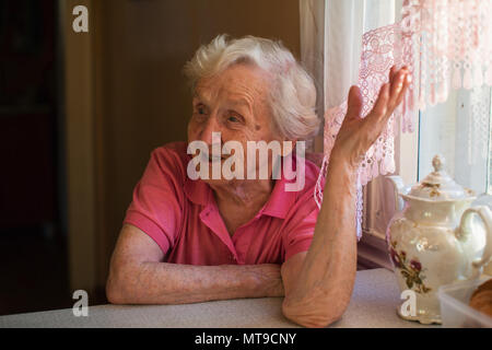 Ältere Frau sitzt am Küchentisch. Stockfoto