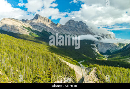 Imposante Panoramablick über den Icefield Parkway entlang der kanadischen Rocky Mountains, Banff nach Jasper. Kuvertieren Wolken stürzen den Grat. Großen Wald. Stockfoto