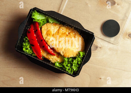 Gegrillte Forelle mit Reis und Kirschtomaten in schwarz Brotdose auf hölzernen Hintergrund Stockfoto