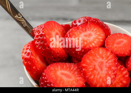 Auf Erdbeeren im Kreise schneiden Detail, aus weisser Keramik Schüssel mit silbernen Löffel. Stockfoto