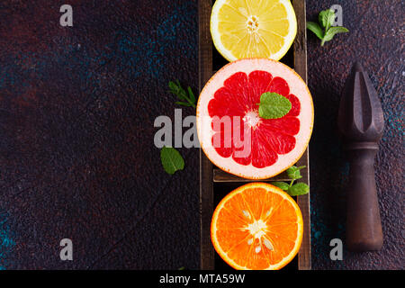 Orange, Zitrone und Grapefruit bunte Scheiben mit Zitrusfrüchten Reibahle auf dunklem Hintergrund, Falt legen Szene Stockfoto