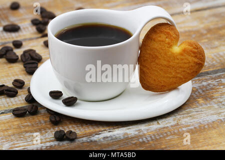 Herzförmige cookie lehnte sich gegen weiße Tasse Kaffee auf Holzmöbeln im Landhausstil Oberfläche Stockfoto