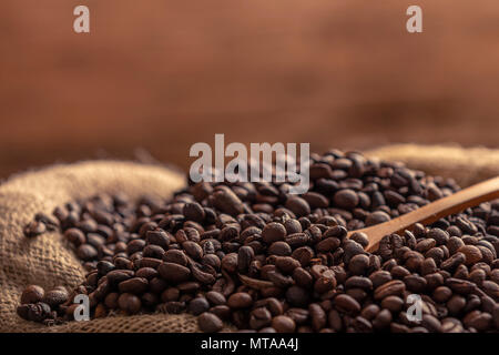 Nahaufnahme der Sack von verschüttetem Kaffee aus frisch gemahlenen Bohnen mit Holzlöffel auf braunem Hintergrund Stockfoto