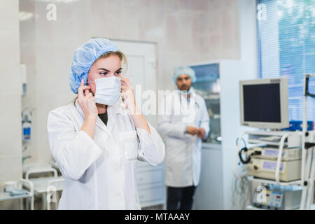 Team von Ärzten wird für den Betrieb vorbereitet. Die Krankenschwester assistant das Tragen der Maske. Arzt Vorbereitung Ausrüstung auf dem Hintergrund. Konzept der Gesundheit, Arbeit im Krankenhaus. Stockfoto