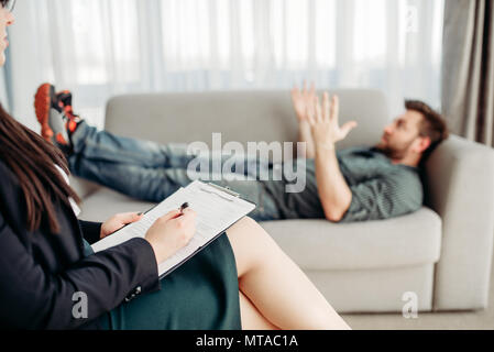 Wütend männlicher Patient an Psychologen, Rezeption, Stress. Ärztin schreibt Notizen in Notepad, professionelle Psychologie Stockfoto