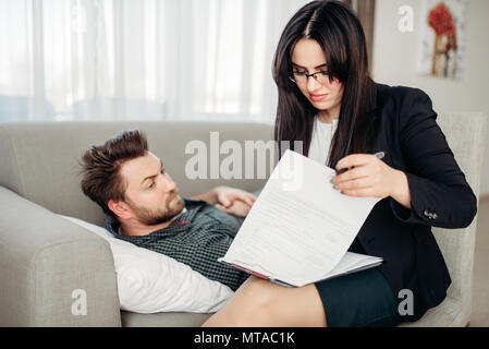 Deprimiert Mann liegt auf Sofa bei psychotherapeut Rezeption. Ärztin schreibt Notizen in Notepad, professionelle Psychologie Unterstützung Stockfoto
